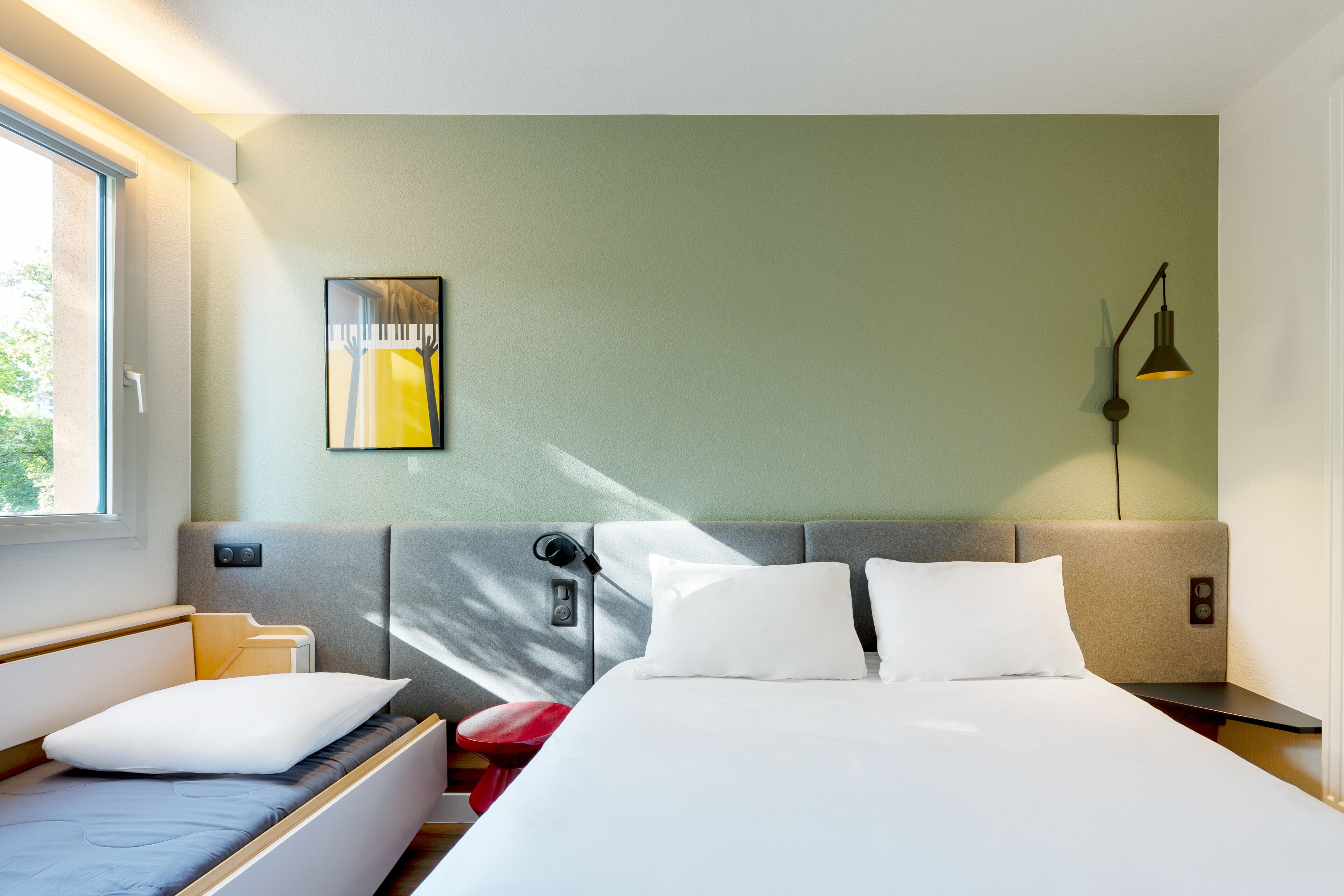 Een moderne hotelkamer met een bed, een nachtkastje, een lamp, een raam en een kunstwerk aan de muur.