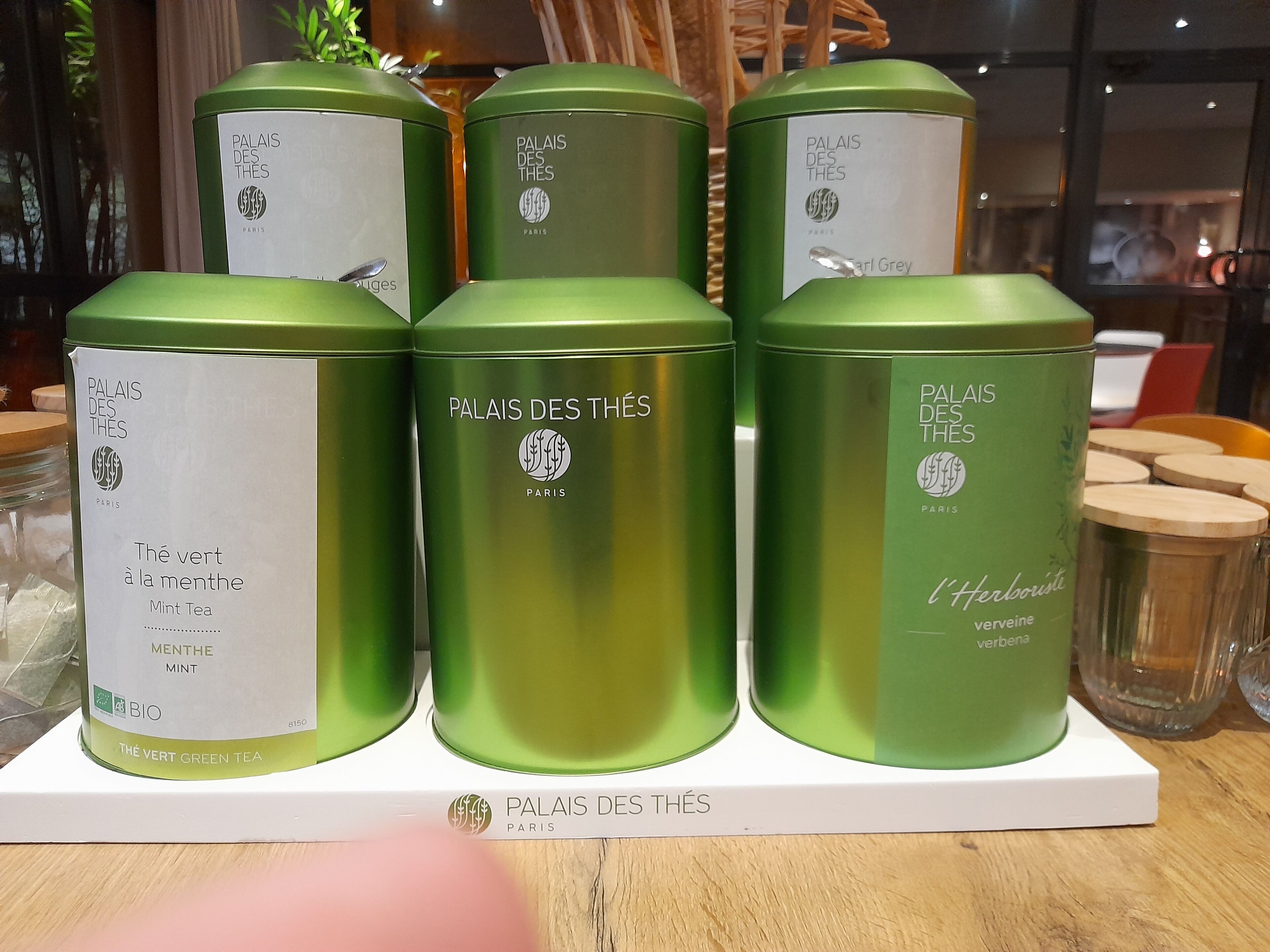 Exhibición de latas de té verde con etiquetas que indican 'Palais Des Thés' y 'París'.