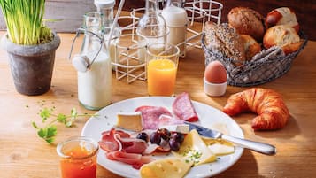 Une table mise pour le petit-déjeuner avec une assiette de fromage, de charcuterie et de pain, ainsi que des bouteilles de lait et un croissant.