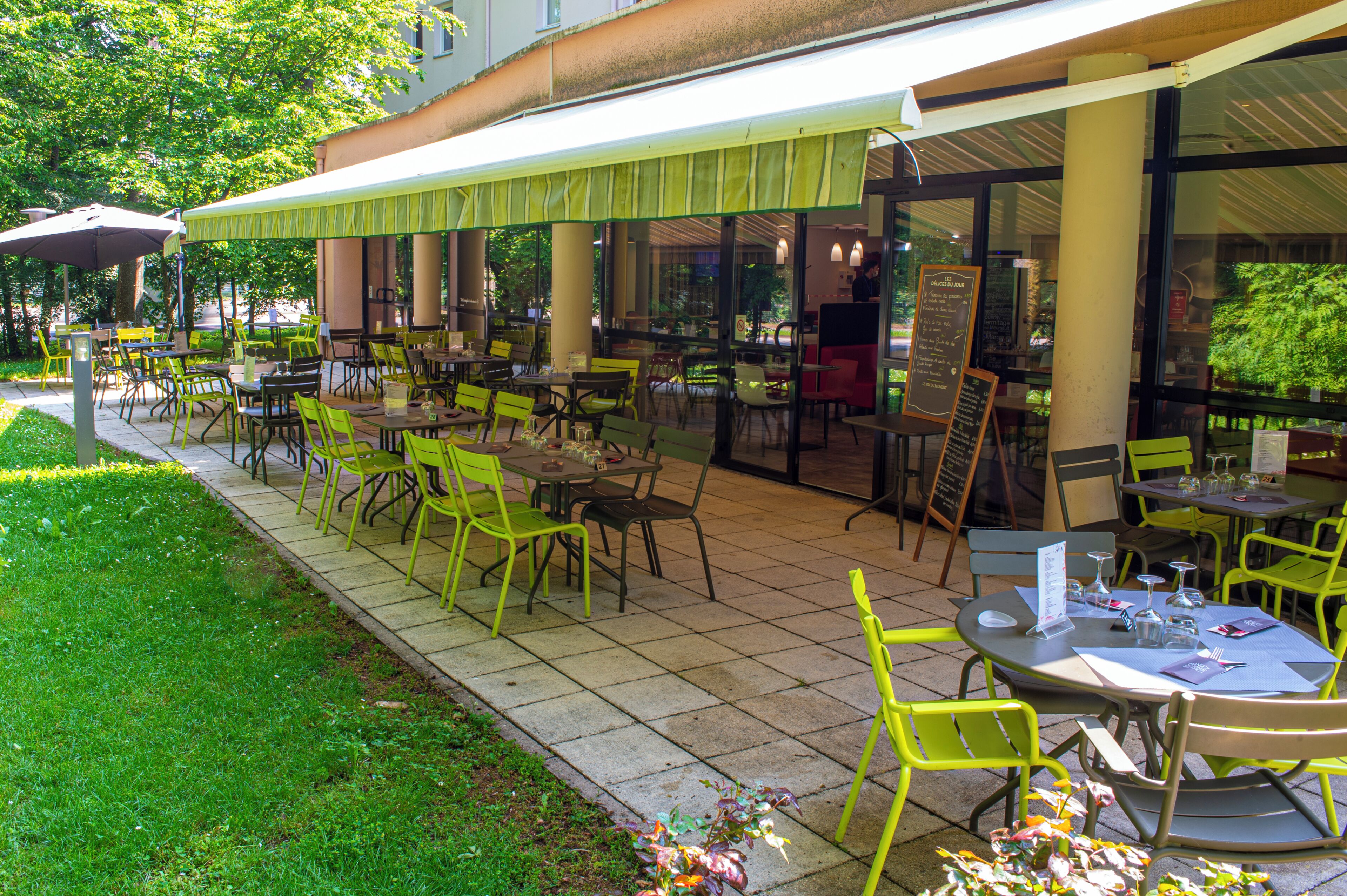An outdoor cafe with tables and chairs, a covered seating area, and a view of the street.