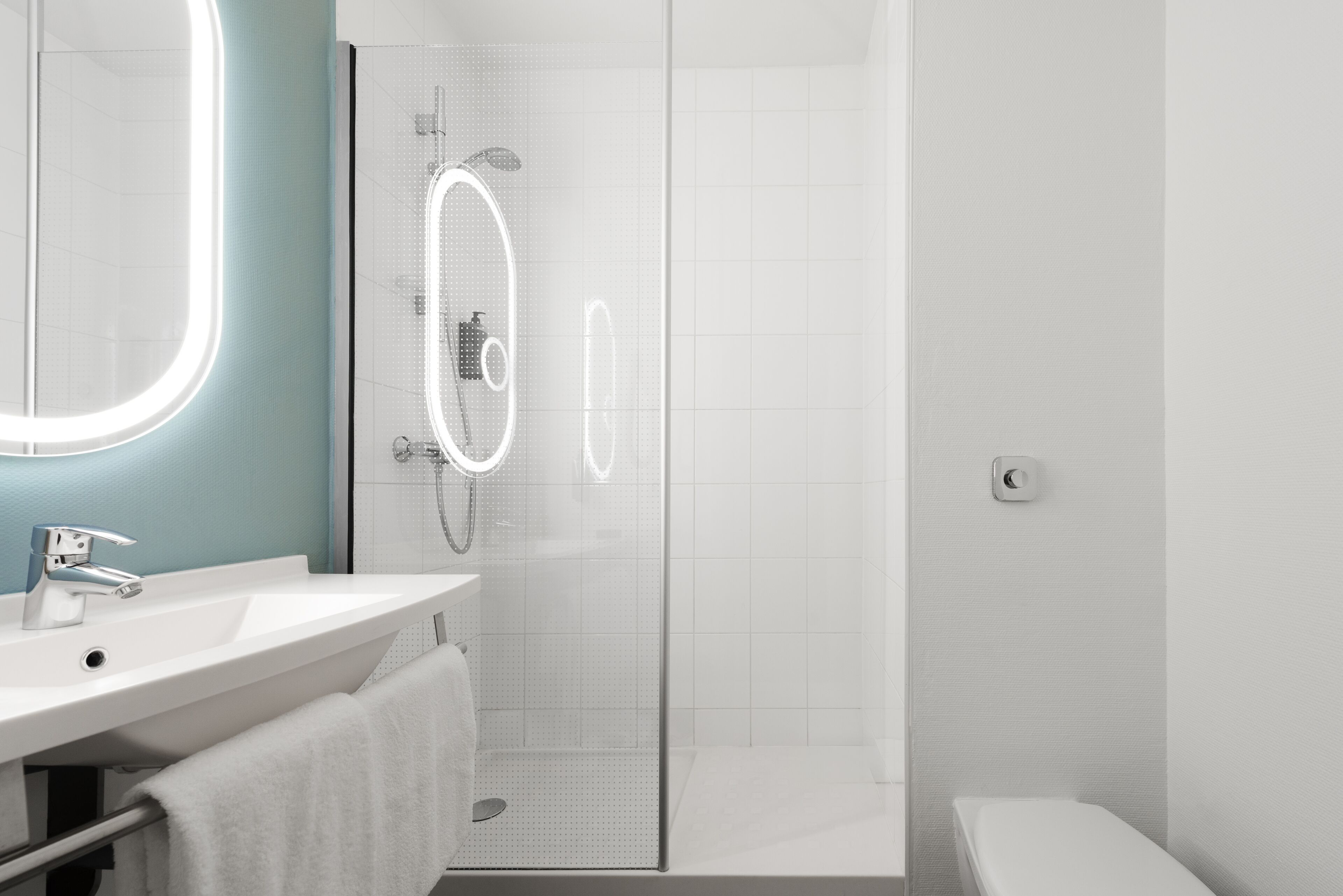 A modern bathroom with a glass-enclosed shower, a white sink, and a mirror with illuminated edges.