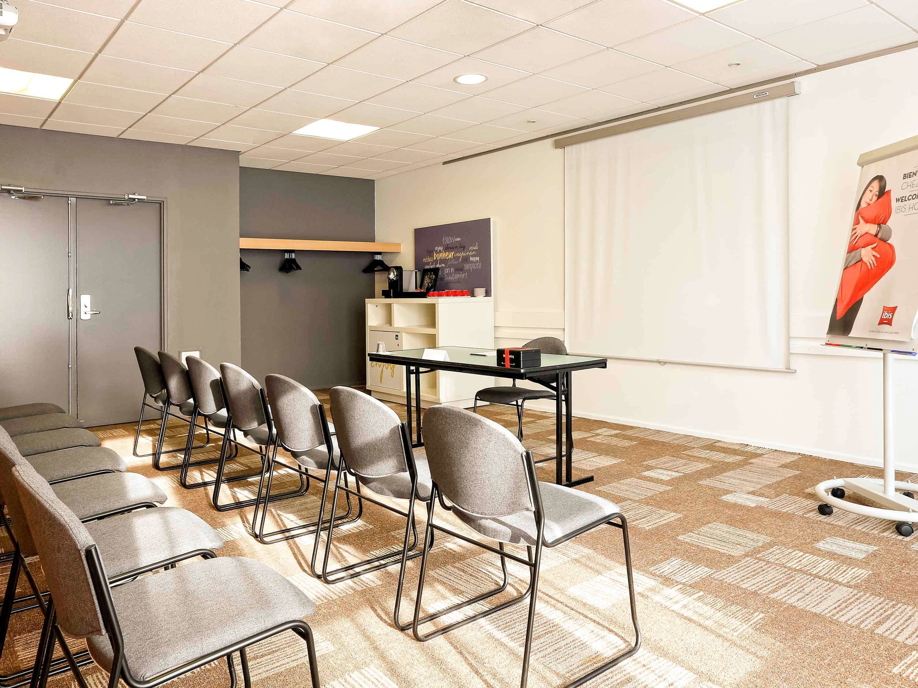 A conference room with a long table, multiple chairs, a projector screen, and a whiteboard.