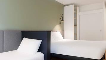 Ett modernt hotellrum med två separata sängar, en garderob och en sänglampa.