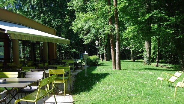 Un área de comedor al aire libre con mesas y sillas, rodeada de árboles.