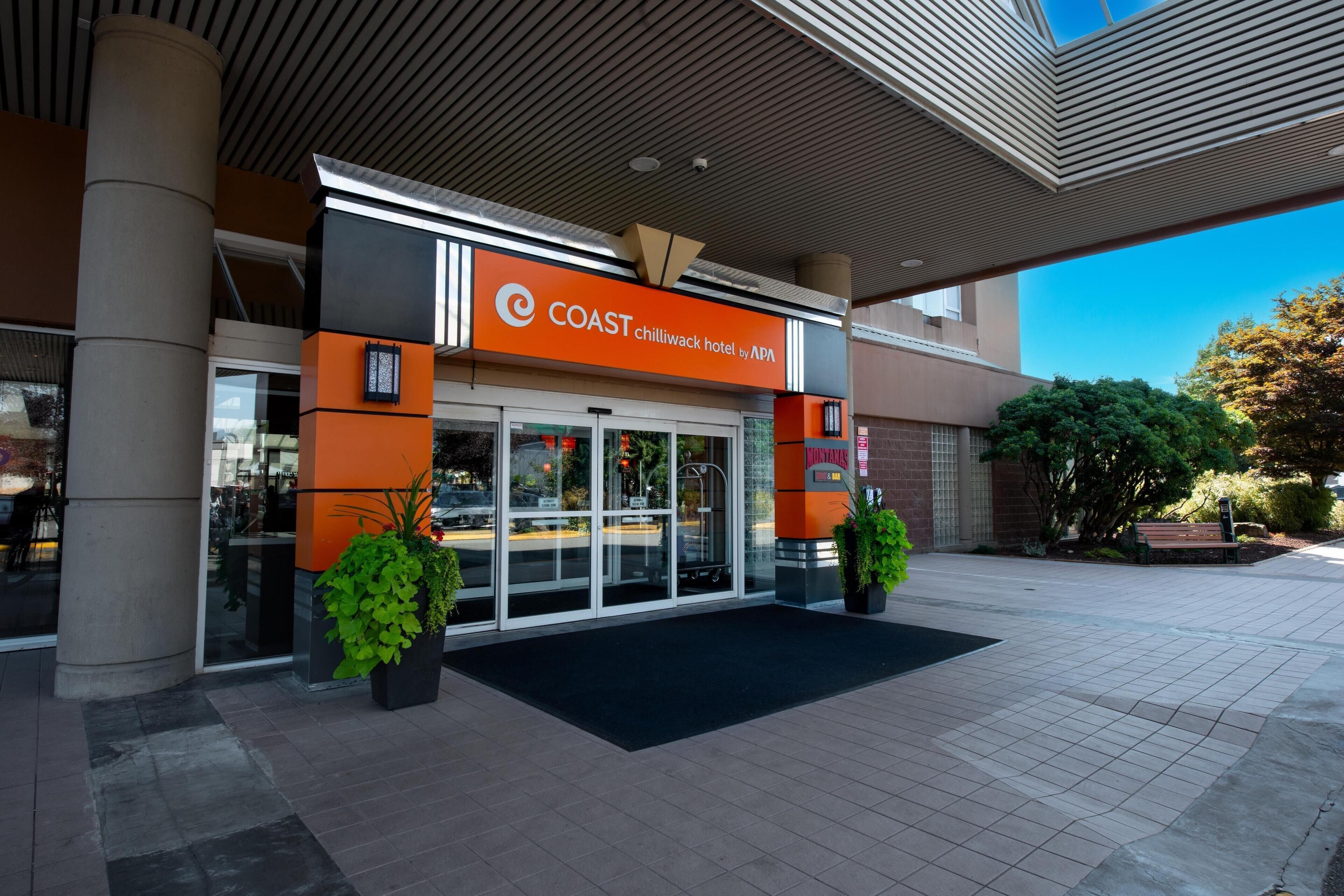 El exterior del Hotel Coast Chillivack de APA, con una fachada moderna, una entrada de cristal y un área de entrada ajardinada.