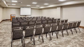 Un salón de conferencias con filas de sillas, una pantalla para proyector y un atril.
