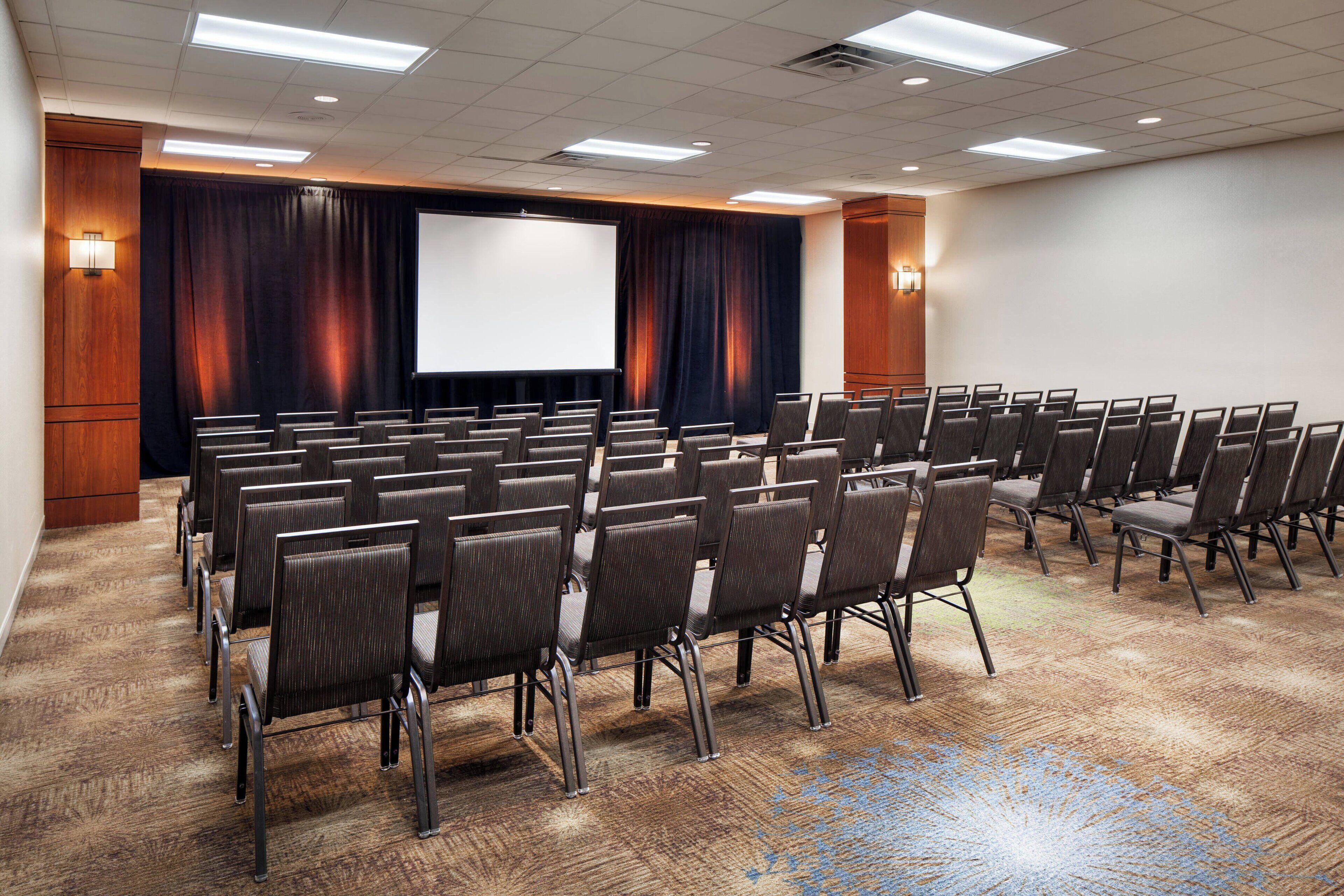A conference room with rows of chairs, a large screen, and a carpeted floor.
