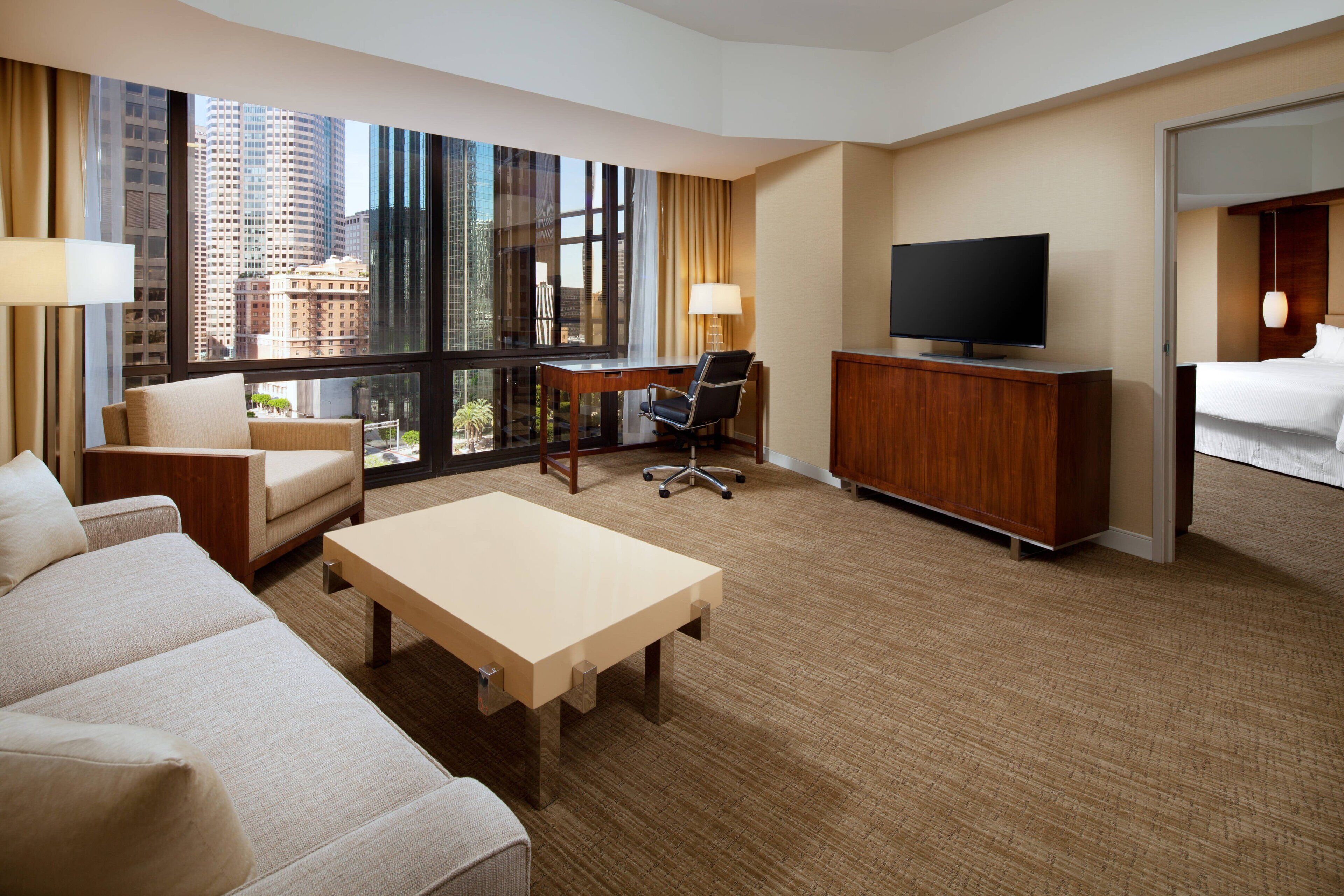 Quarto de hotel com uma janela grande, televisão de tela plana, escrivaninha, cadeira, cama e sofá.