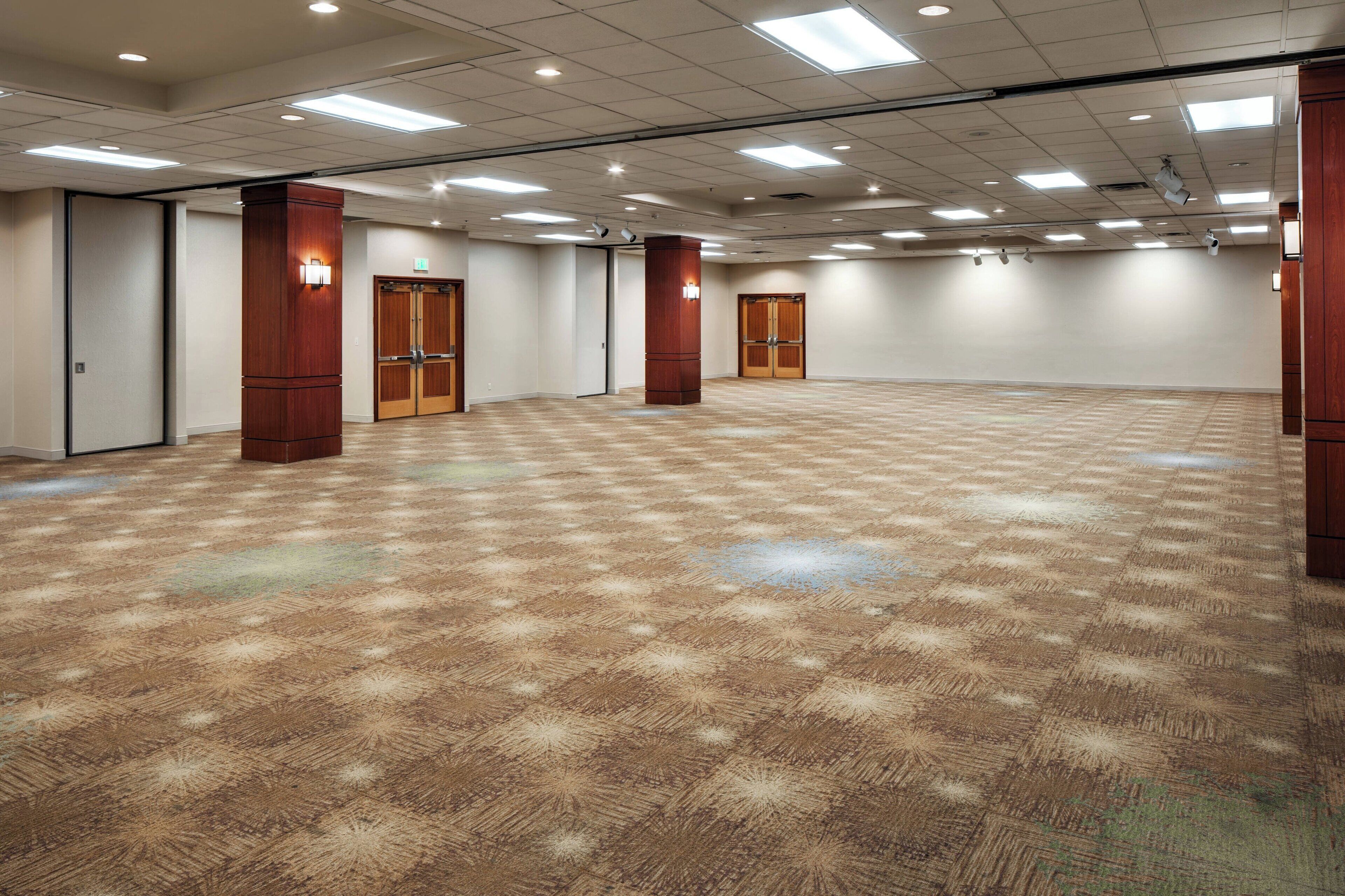 A large, empty conference room with a checkered carpet, wooden doors, and recessed lighting.