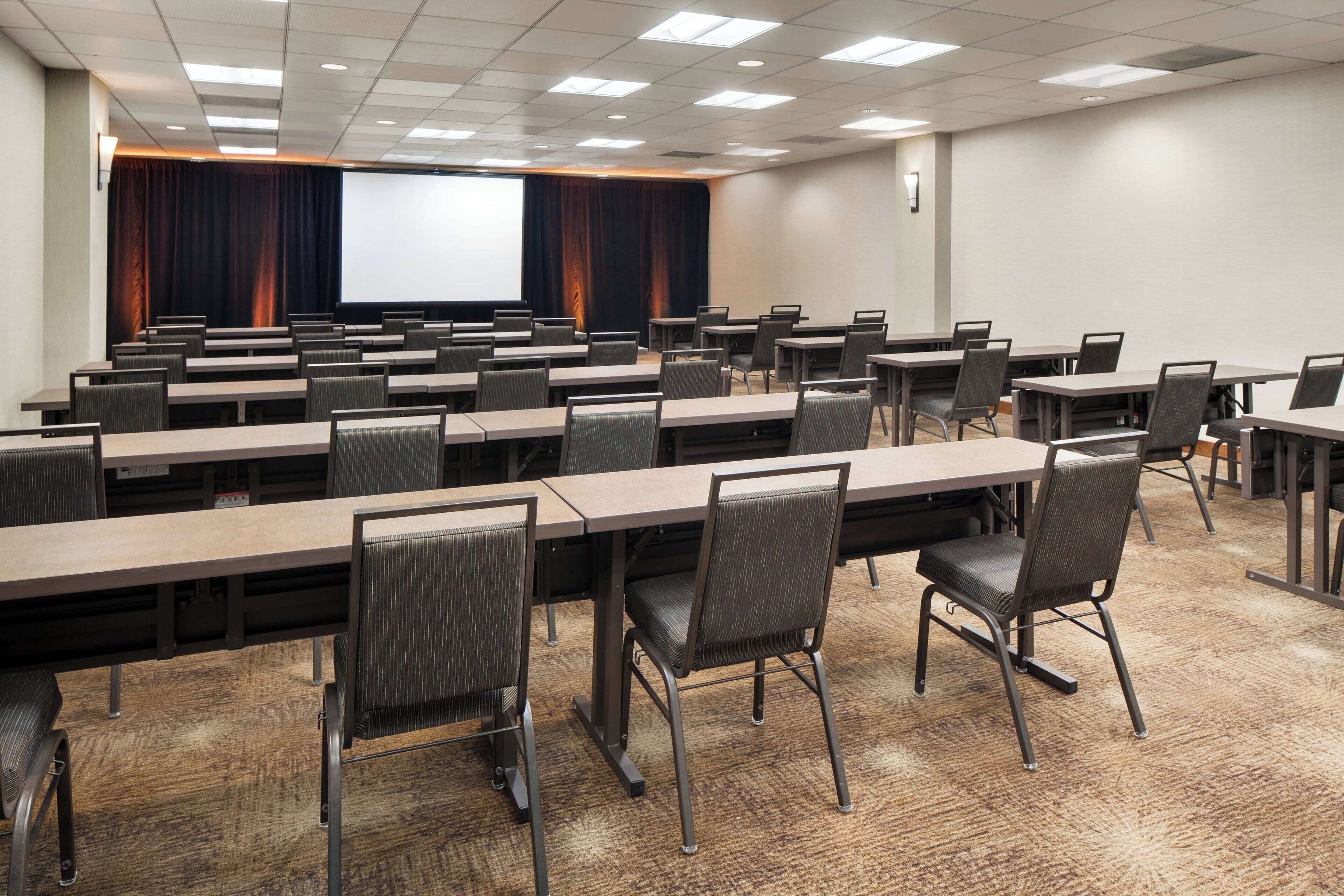 A conference room with multiple tables and chairs, a large screen, and a projector.