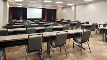 A conference room with multiple tables and chairs, a large screen, and a projector.