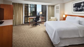 Une chambre d’hôtel avec un grand lit, un bureau, une chaise et une vue sur la ville par la fenêtre.