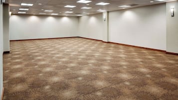 Een ruime, lege congreszaal met een patroon vloerkleed, witte wanden en een plafond met inbouwverlichting.