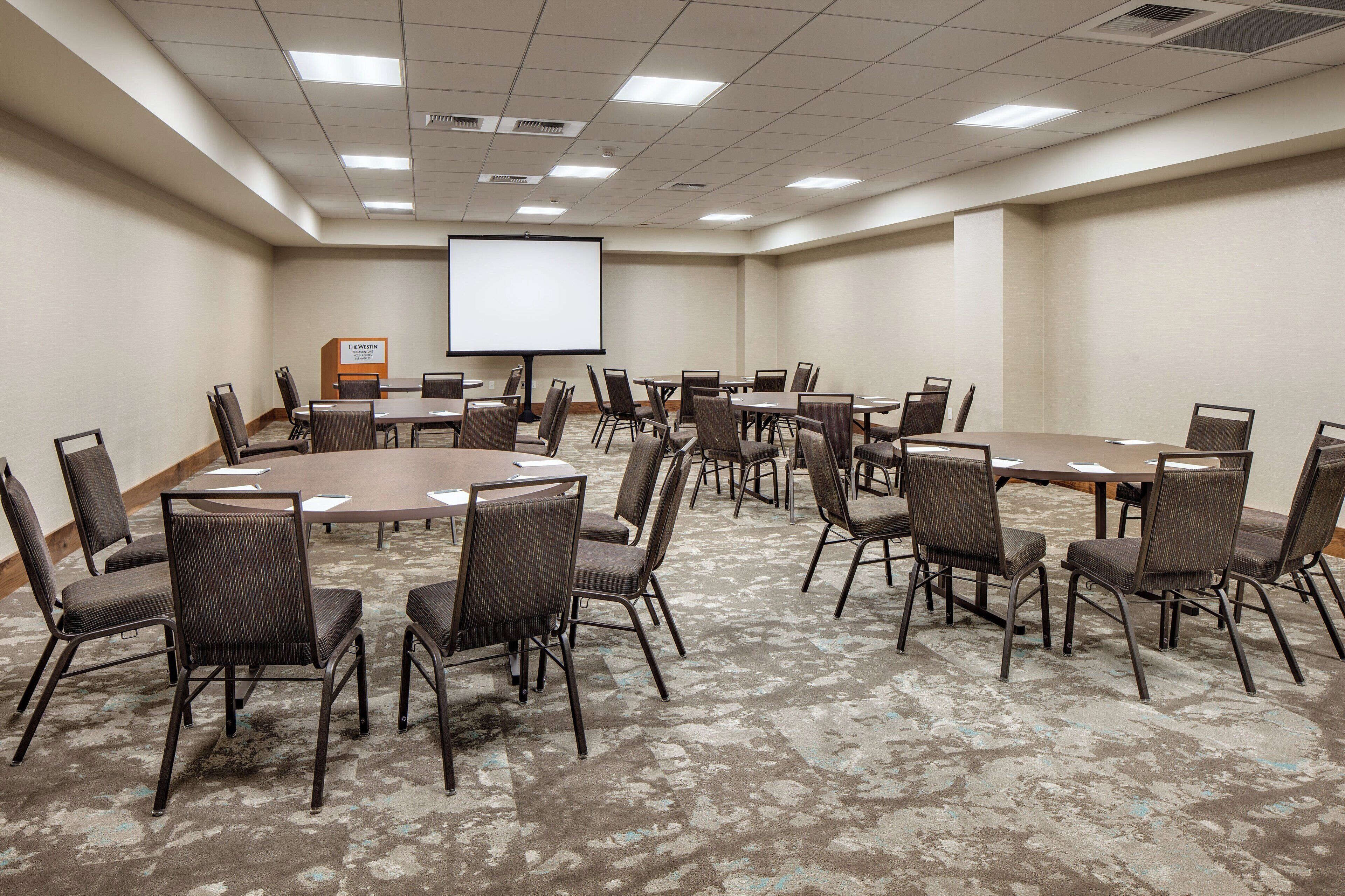 A conference room with a large screen, multiple tables, and chairs arranged for meetings.
