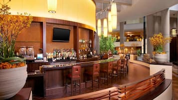 A modern bar area with a curved counter, multiple bar stools, and a large potted plant.