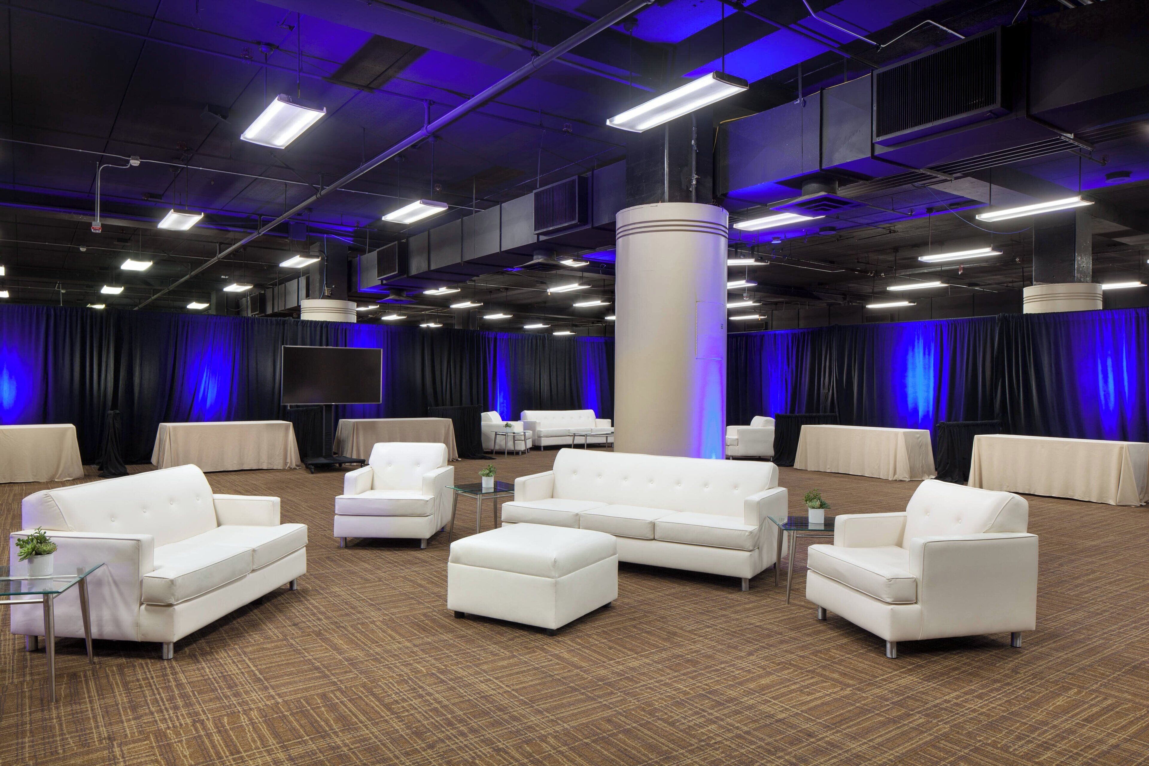 A spacious room with white sofas and a large pillar, featuring a carpeted floor and blue lighting.