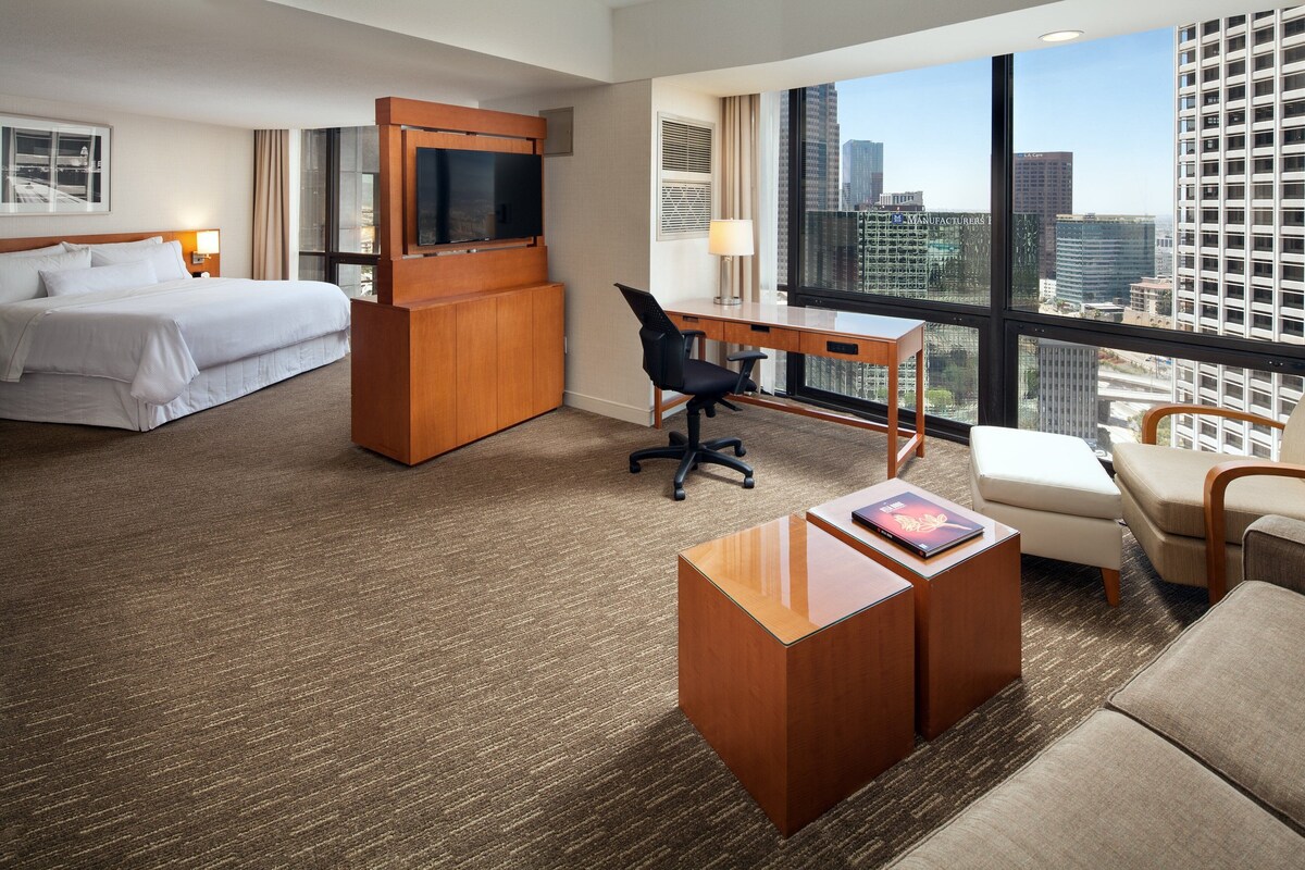 A hotel room with a bed, desk, and city view.