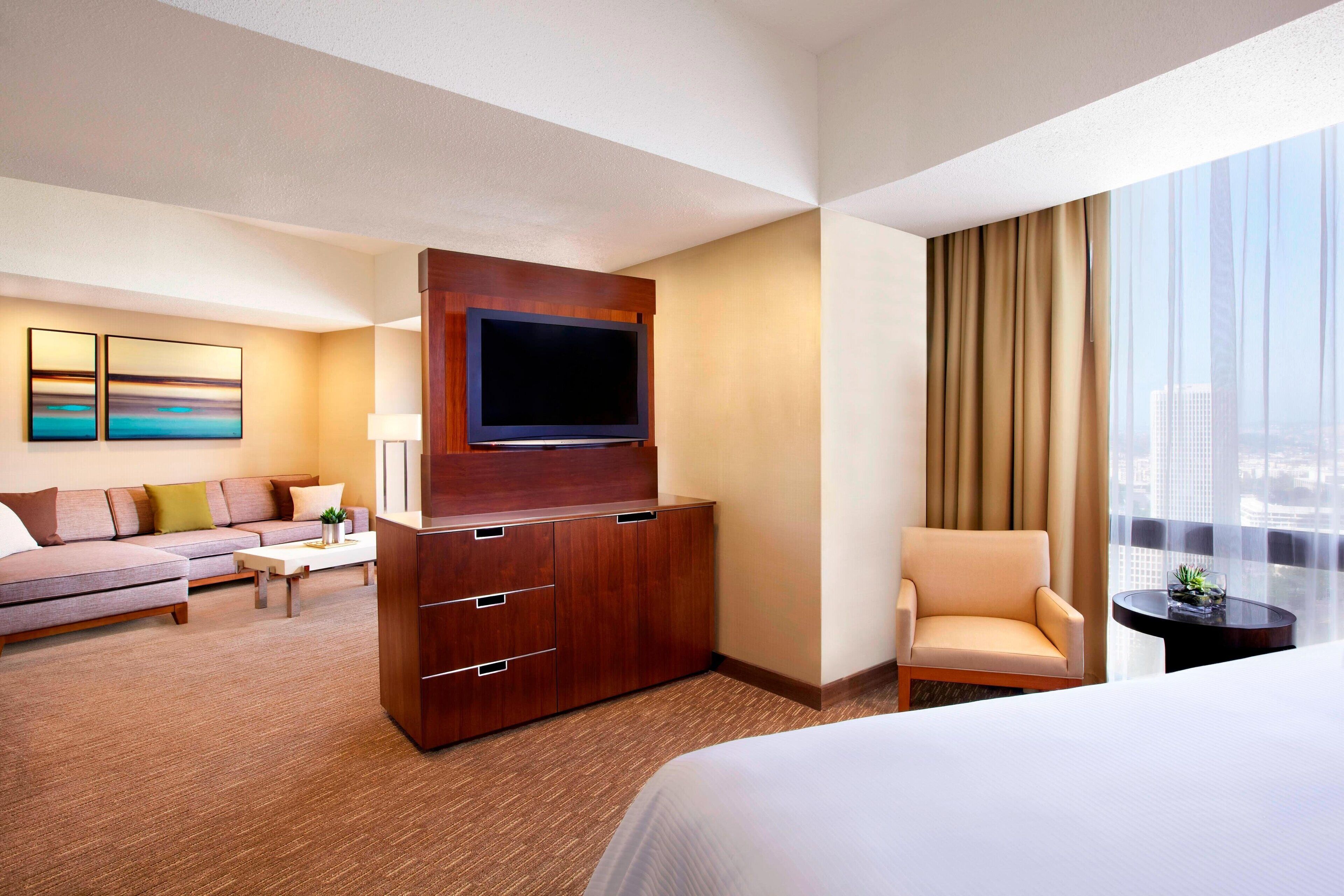 A hotel room with a large bed, a sofa, a TV mounted on a wooden cabinet, a chair, and a small table.