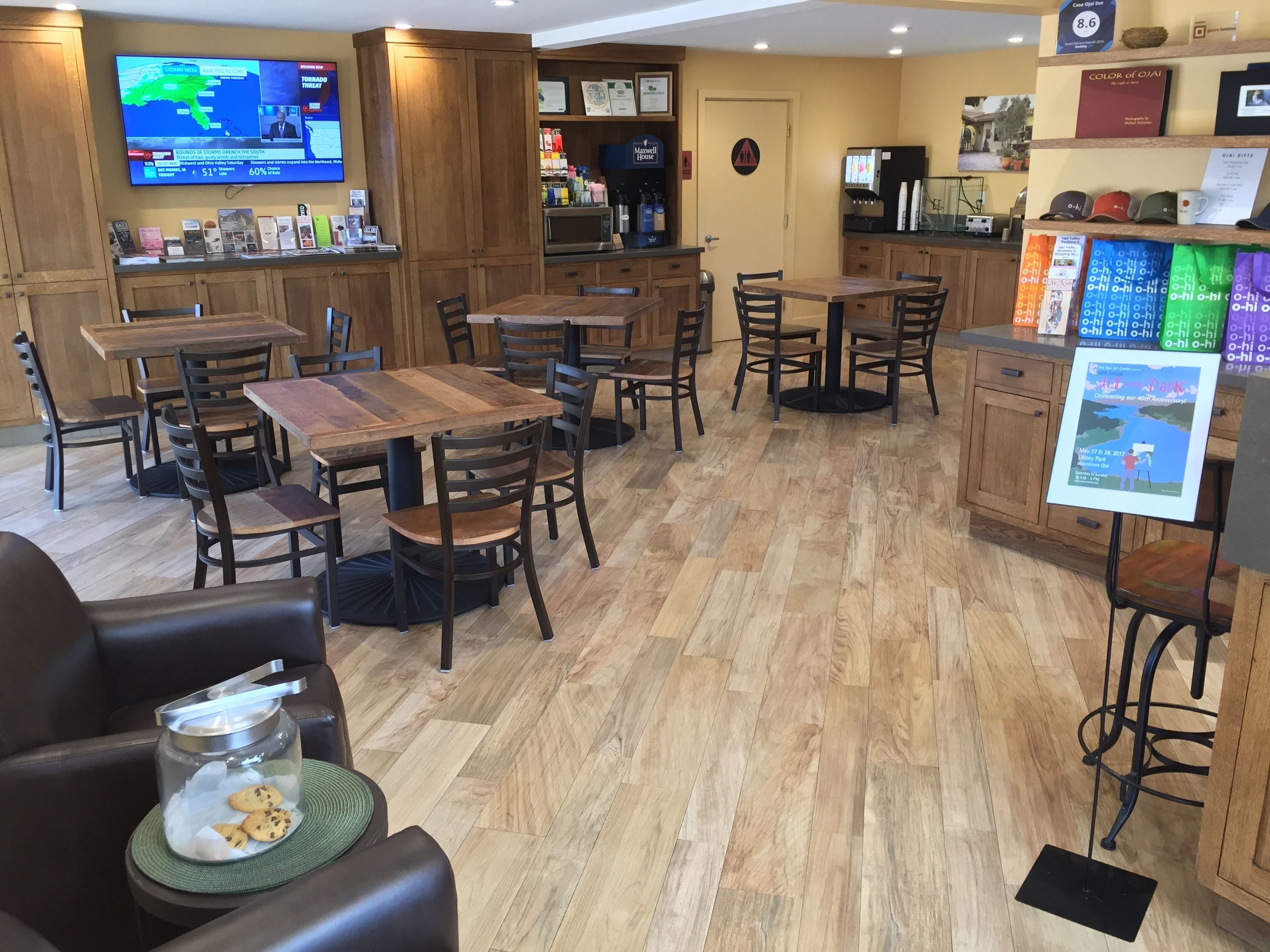 Un restaurante con mesas y sillas de madera, un televisor mostrando noticias y una máquina de café.