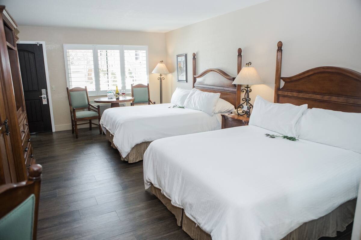 Quarto de hotel com duas camas, uma cadeira, uma mesa com uma garrafa e um abajur.