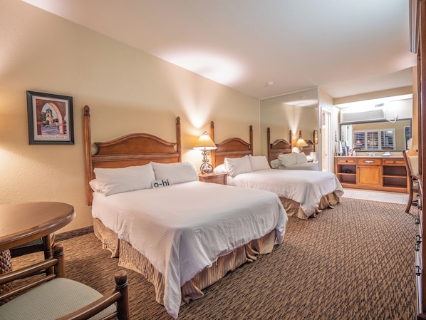 A hotel room with two beds, a wooden headboard, a small table, a chair, a mirror, and a framed picture on the wall.