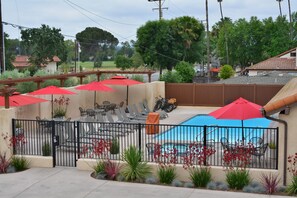 A backyard with a pool, patio furniture, and red umbrellas.