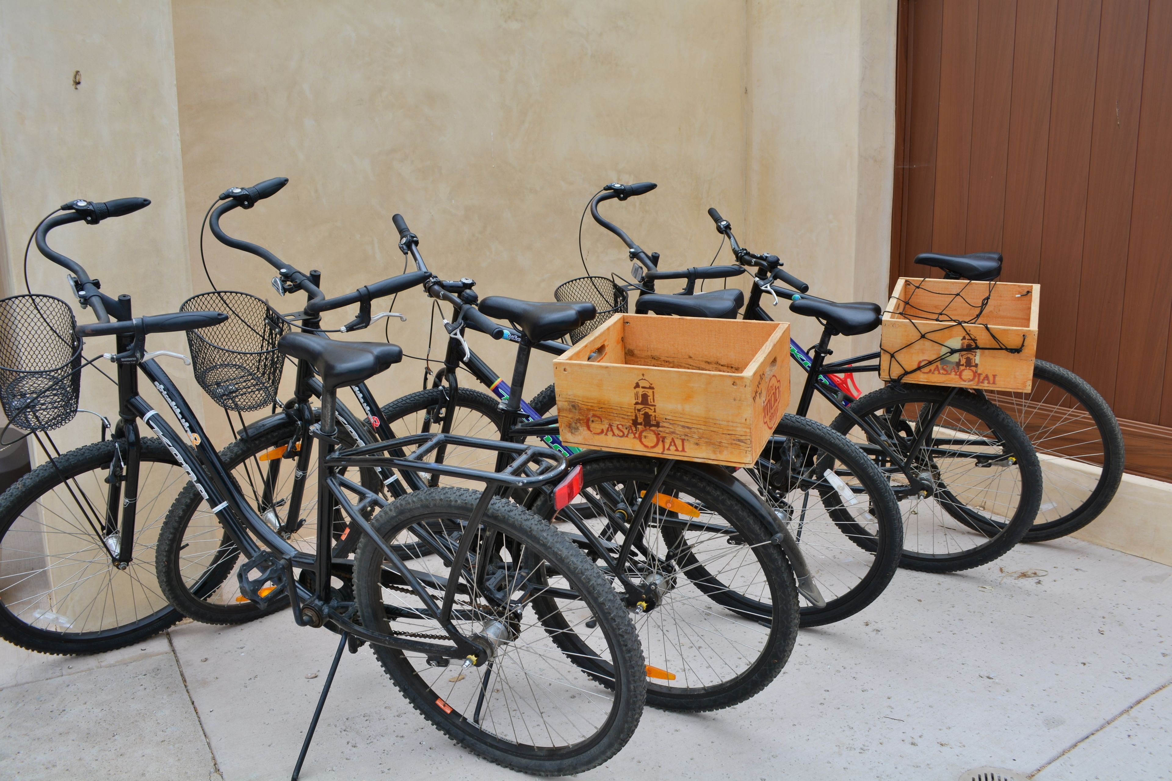 Una fila de bicicletas estacionadas contra una pared, cada una con una caja de madera sujeta en la parte trasera.