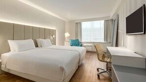 A hotel room with two beds, a desk, a chair, a TV, and a window with curtains.