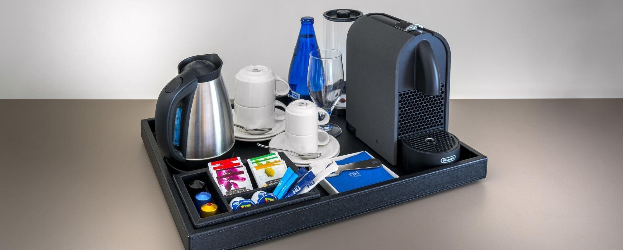 A travel tray with a kettle, coffee maker, glass, and various toiletries.