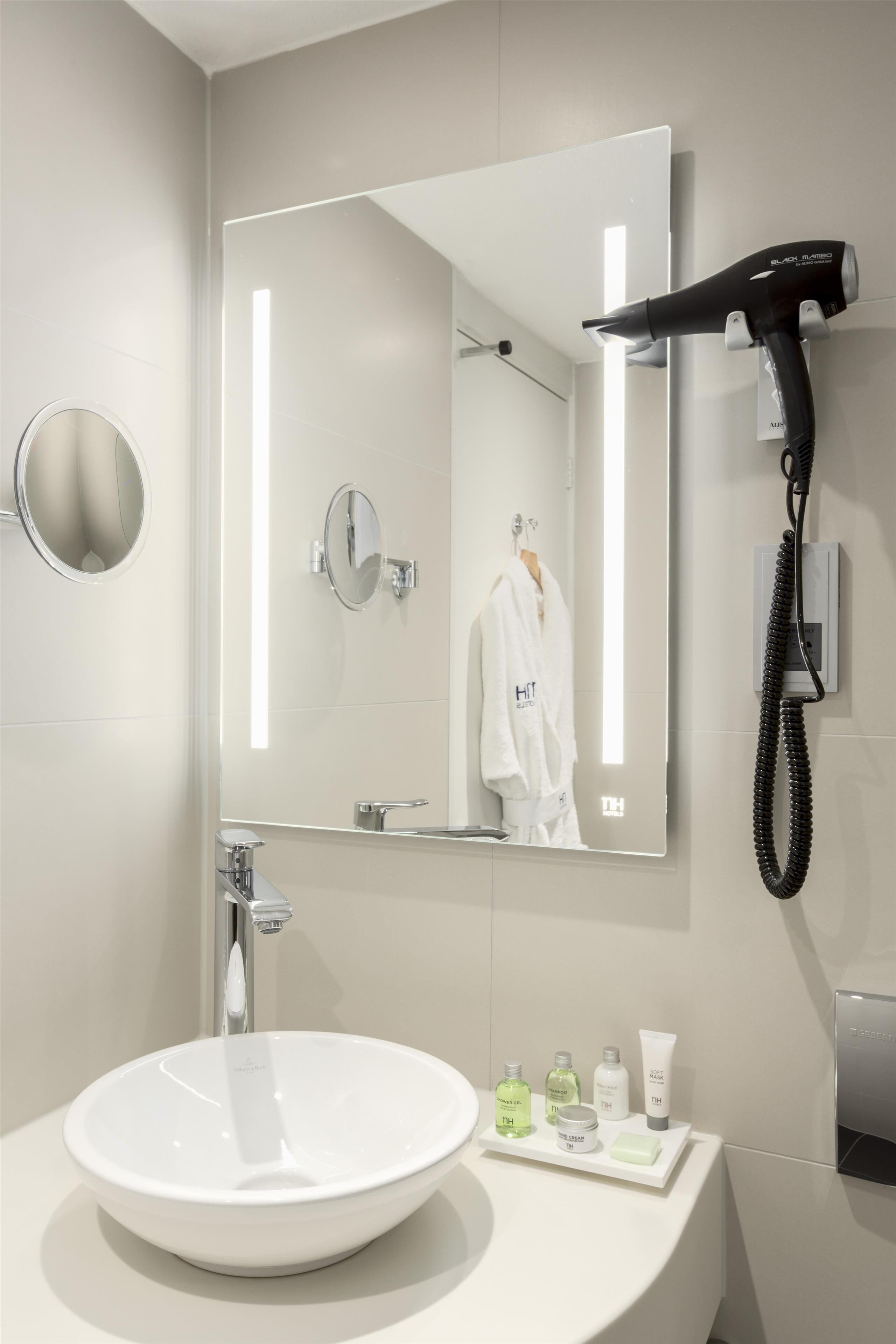 A modern bathroom with a round sink, a large mirror, a hairdryer, and toiletries on the counter.