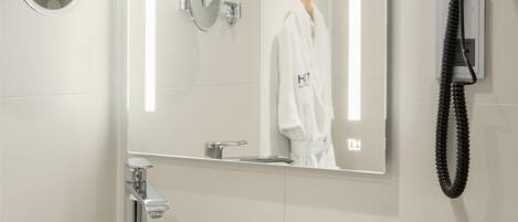 A modern bathroom with a round sink, a large mirror, a hairdryer, and toiletries on the counter.