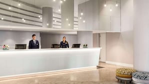 A modern reception area with a long counter, two receptionists, and a seating area with ottomans.