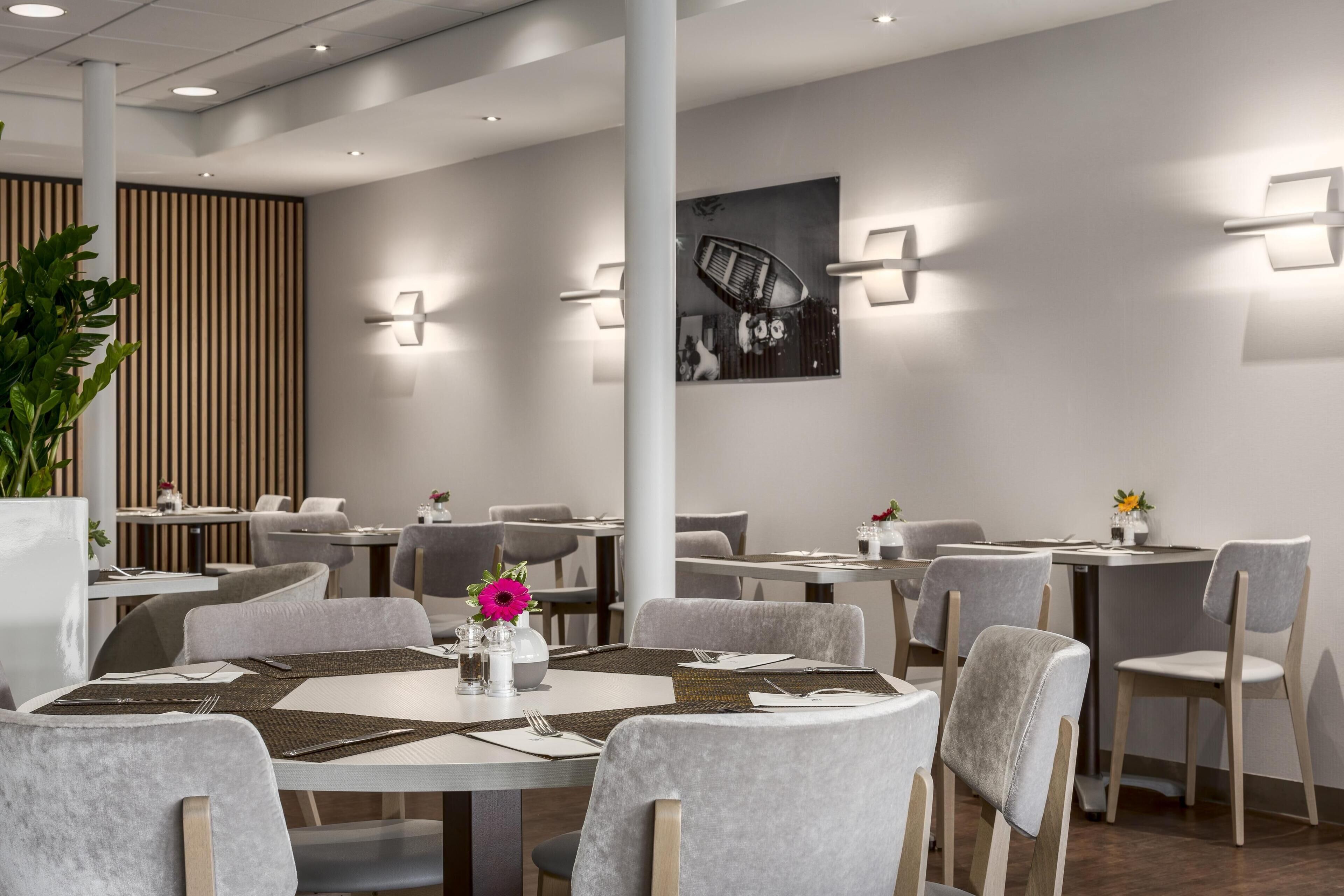 A modern dining area with round tables, grey upholstered chairs, and contemporary wall sconces.