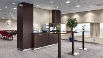 A modern hotel lobby with a reception desk, a coffee machine, a clock, and a large window with a view of the city.