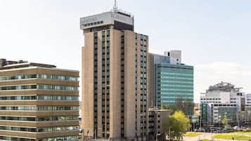 Un moderno edificio de hotel con una antena destacada, rodeado de otros edificios altos.