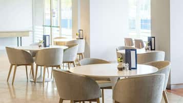 Un comedor moderno con mesas y sillas redondas, ventanas amplias y un techo alto con iluminación lineal.