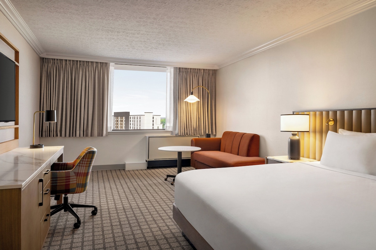 A hotel room with a bed, desk, chair, and a small table.