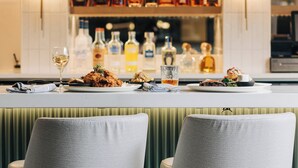 A bar area with a long counter, multiple liquor bottles, and two upholstered bar stools. - Crowne Plaza Louisville Airport Expo Ctr by IHG (Louisville)