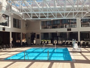 An indoor swimming pool with a high ceiling and skylights, surrounded by lounge chairs and a poolside area. - Crowne Plaza Louisville Airport Expo Ctr by IHG (Louisville)