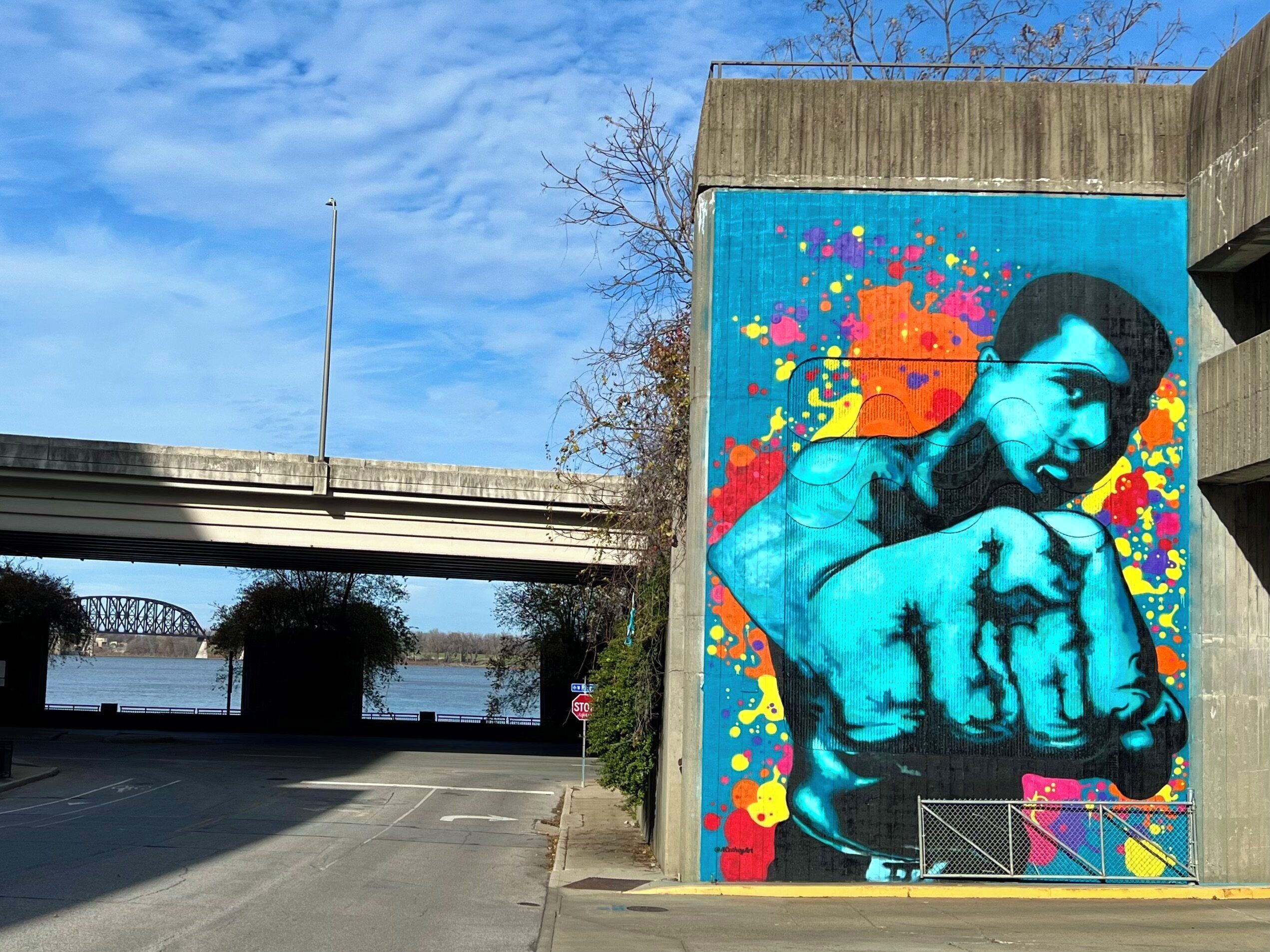 A mural of a person with a clenched fist on a building under a bridge.