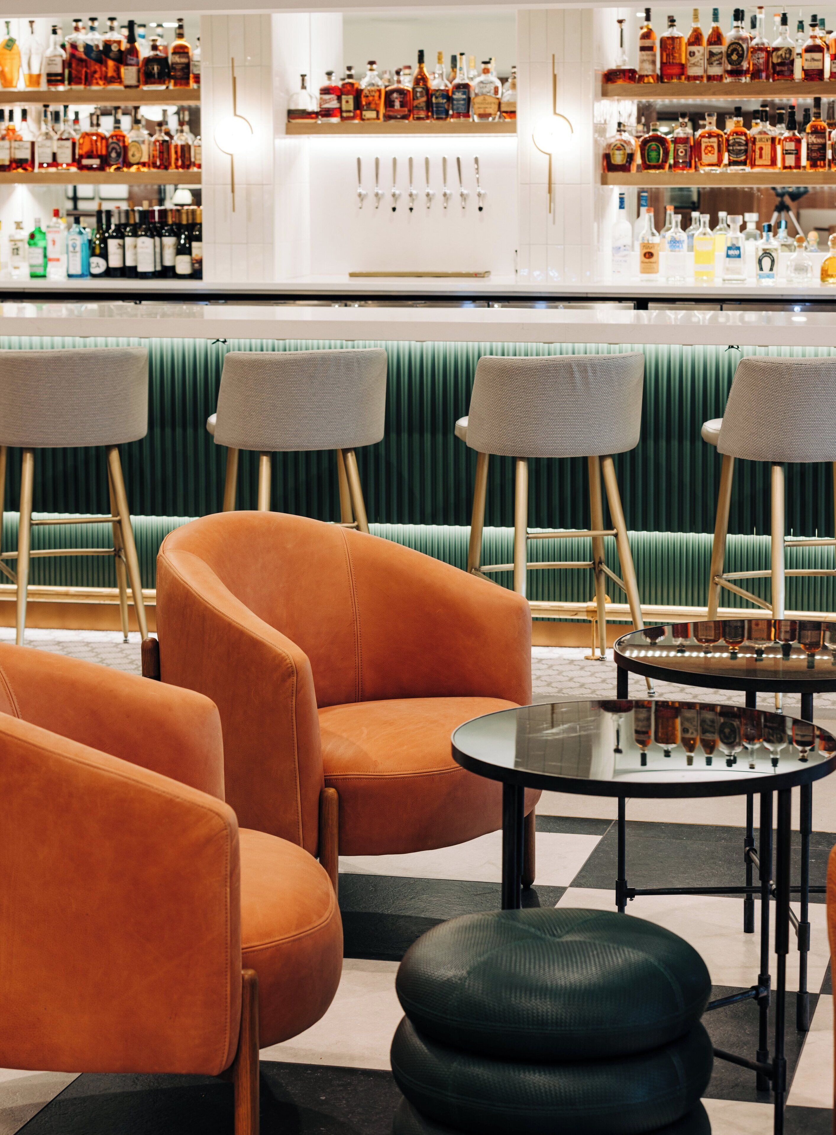 Zona de bar con asientos, incluyendo sillas anaranjadas y una mesa, y estanterías con varias botellas.