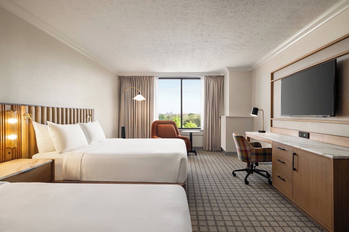 A hotel room with two beds, a desk, a chair, a TV, and a window with curtains.