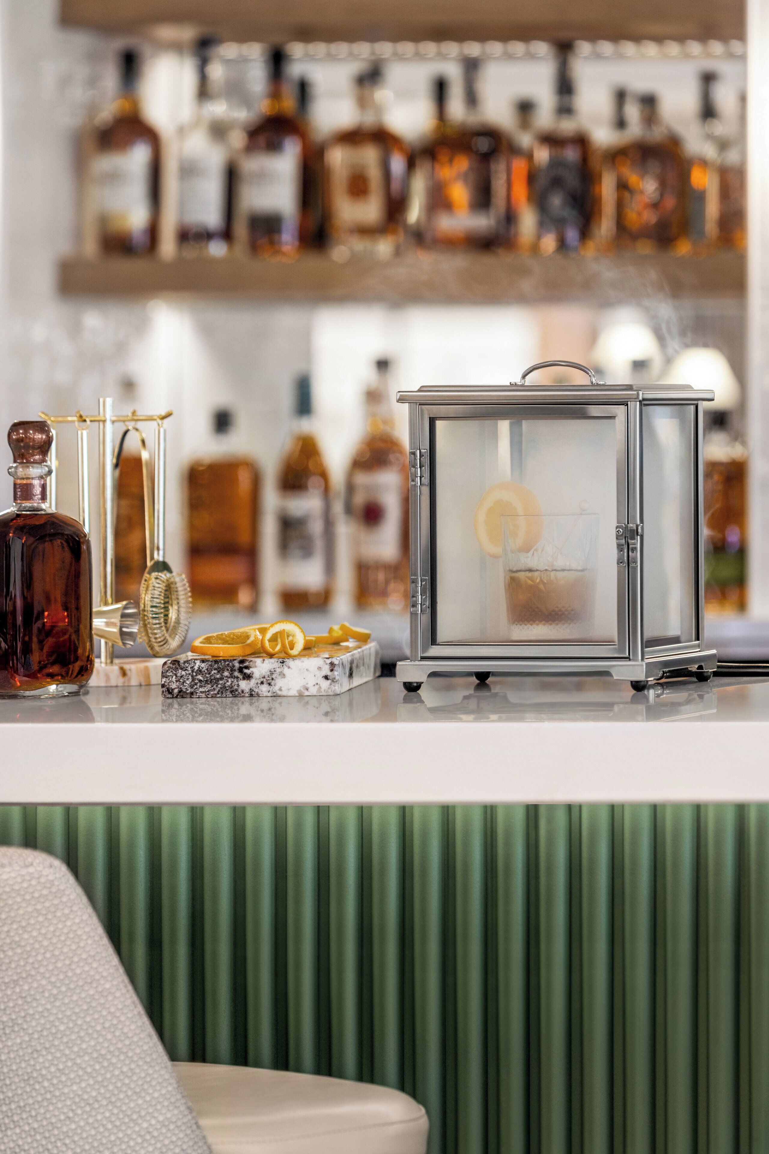 A bar area with a variety of liquor bottles, a clear glass container, and a decorative item on a marble surface.