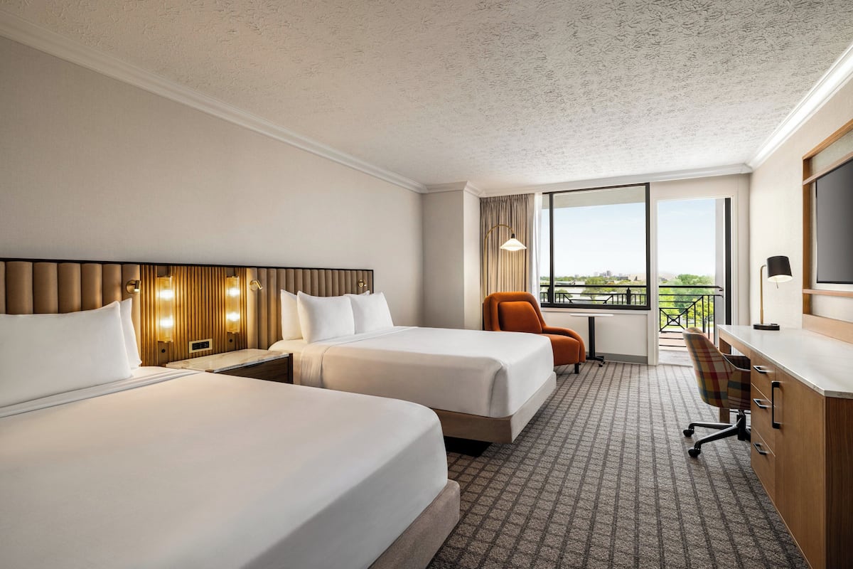 Une chambre d’hôtel avec deux lits, un bureau, une chaise et une grande fenêtre donnant sur un beau paysage.