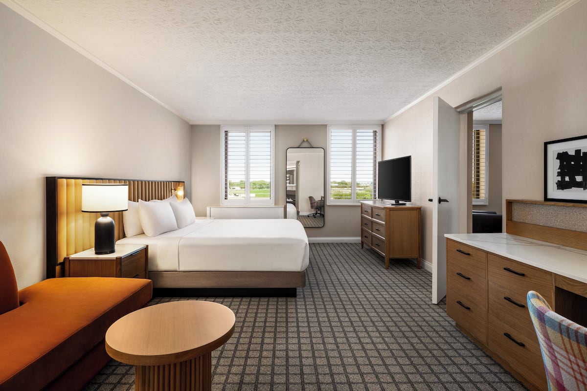 Une chambre d’hôtel équipée d’un lit, d’un bureau, d’une chaise, d’une télévision et d’une fenêtre avec des stores.