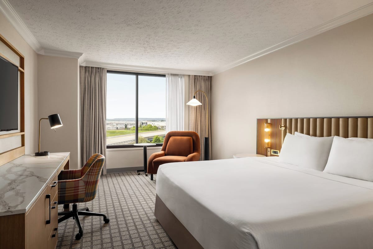 Une chambre d’hôtel avec un grand lit, un bureau avec une chaise, une télévision et une fenêtre avec des rideaux.