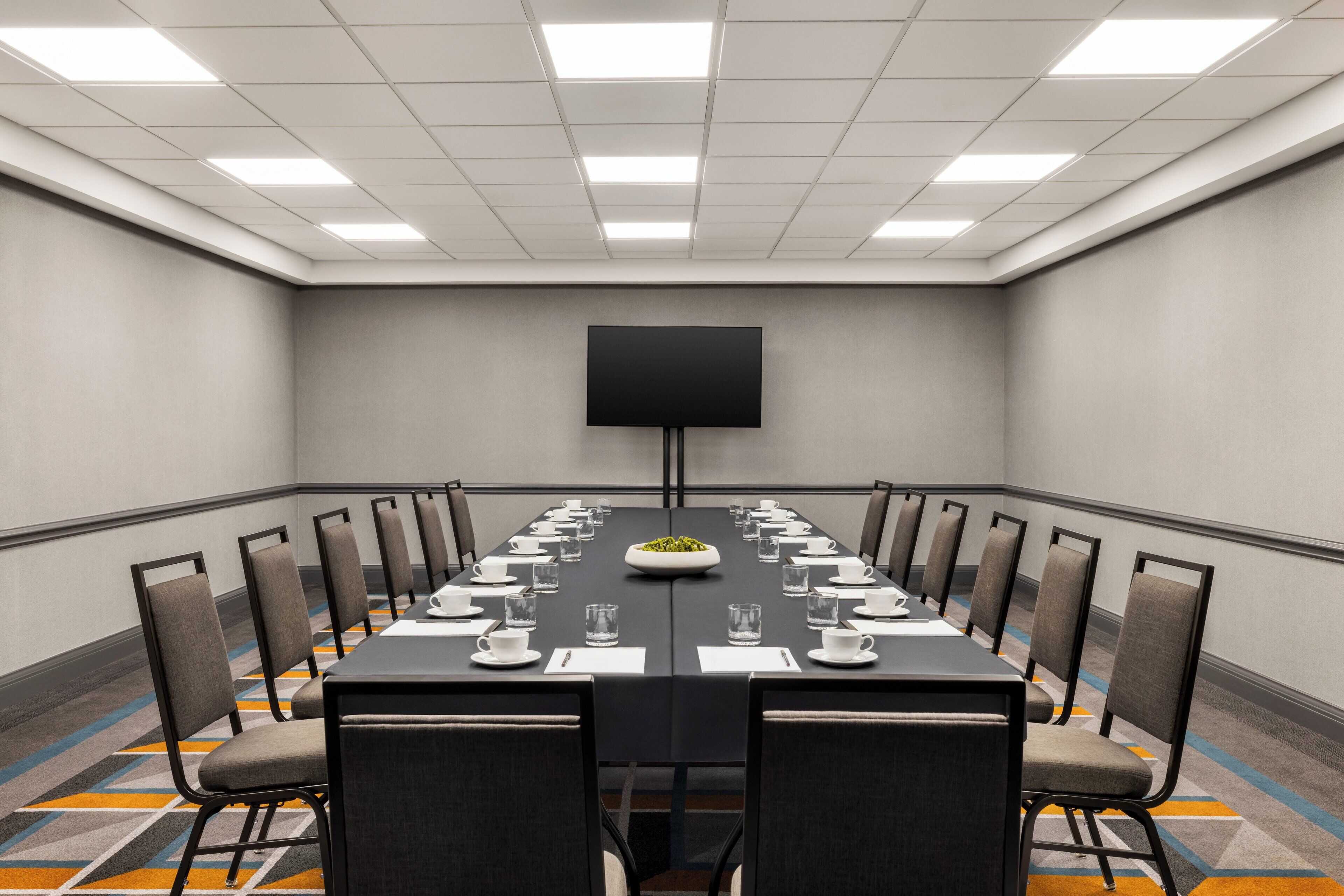 A conference room with a long table, chairs, a flat-screen TV, and a bowl of fruit.