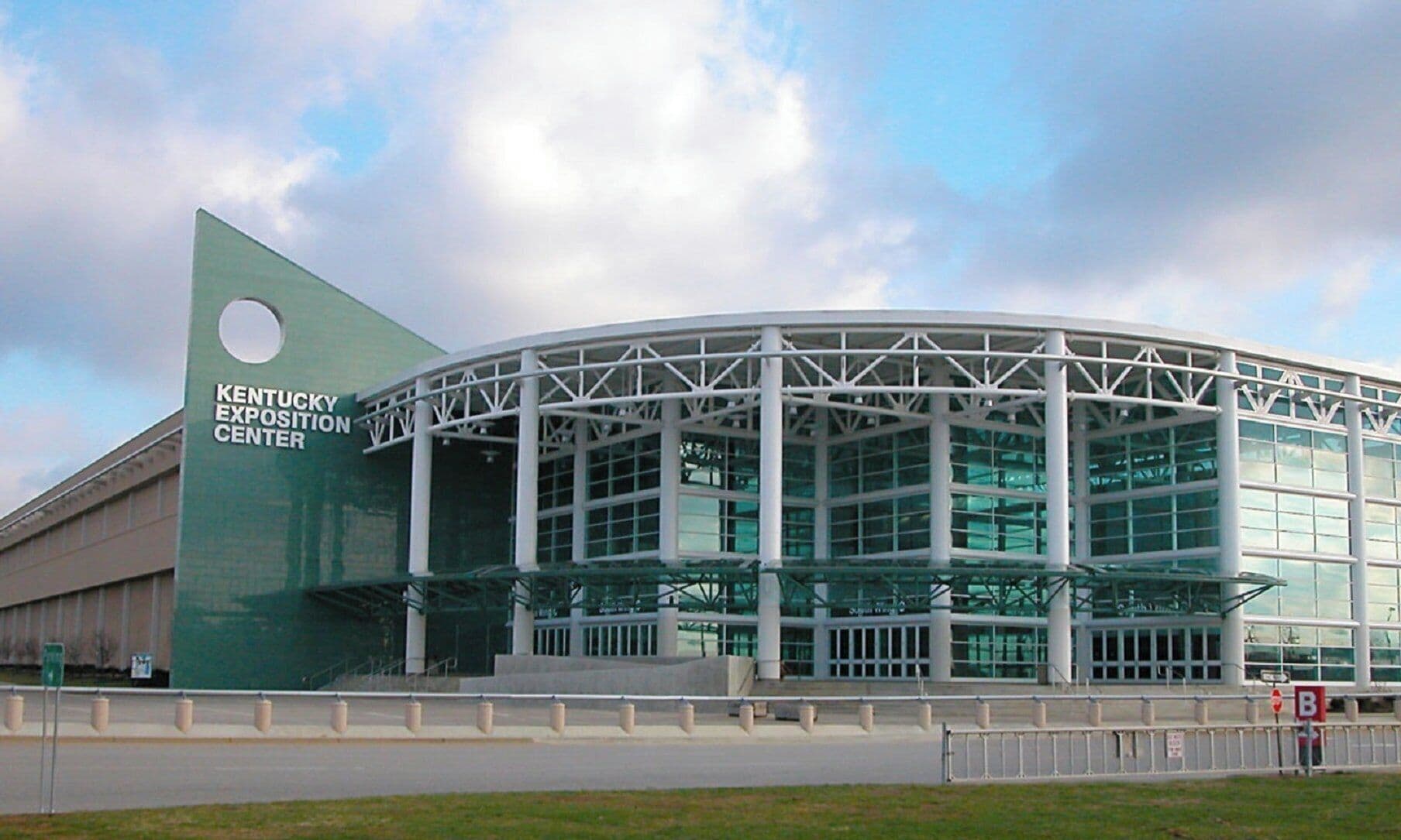 Un edificio moderno con un amplio frente de vidrio y un llamativo letrero verde que dice "Kentucky Exposition Center".