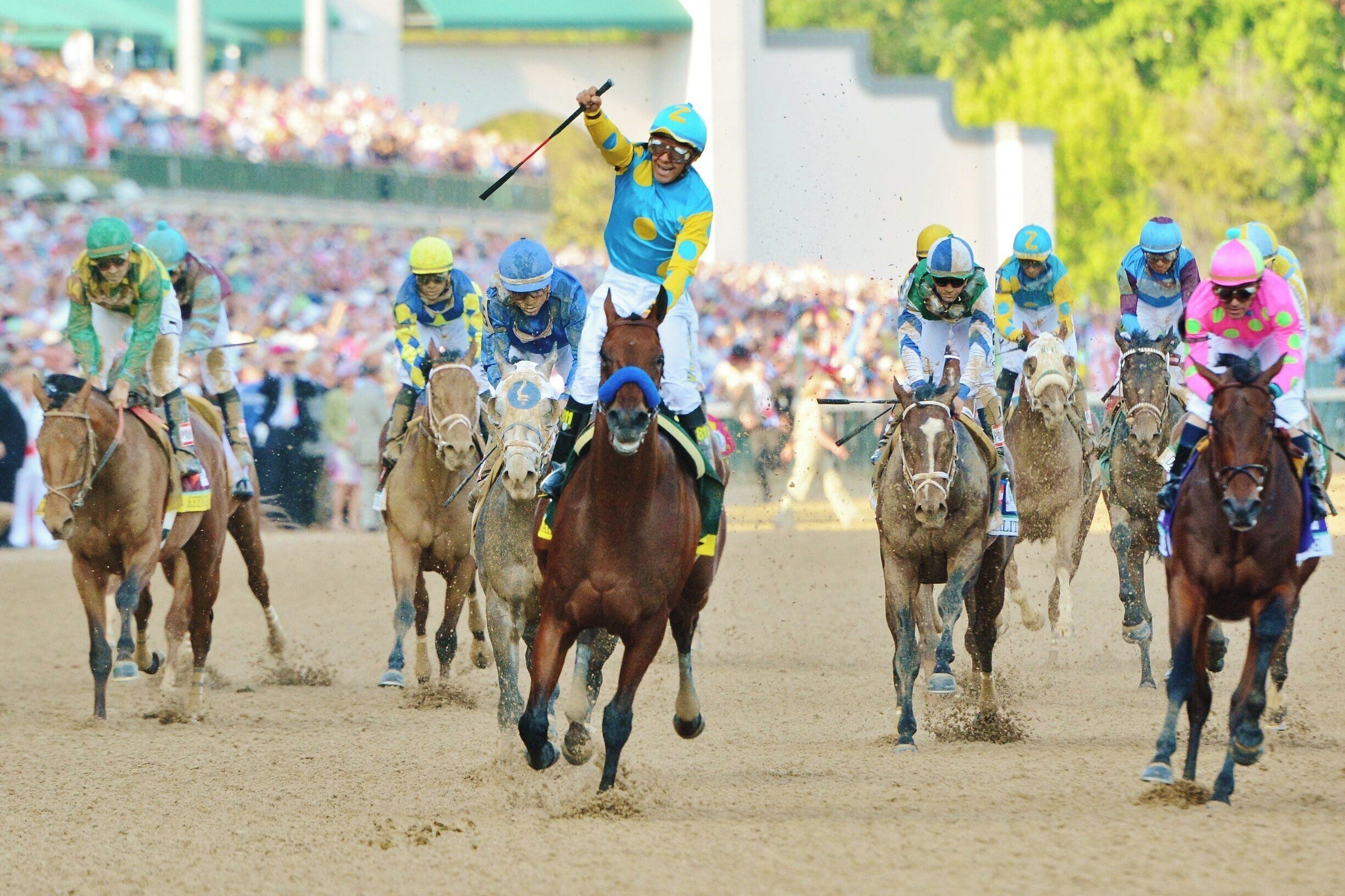 A horse race with jockeys on horses, a crowd in the background, and a sandy track.