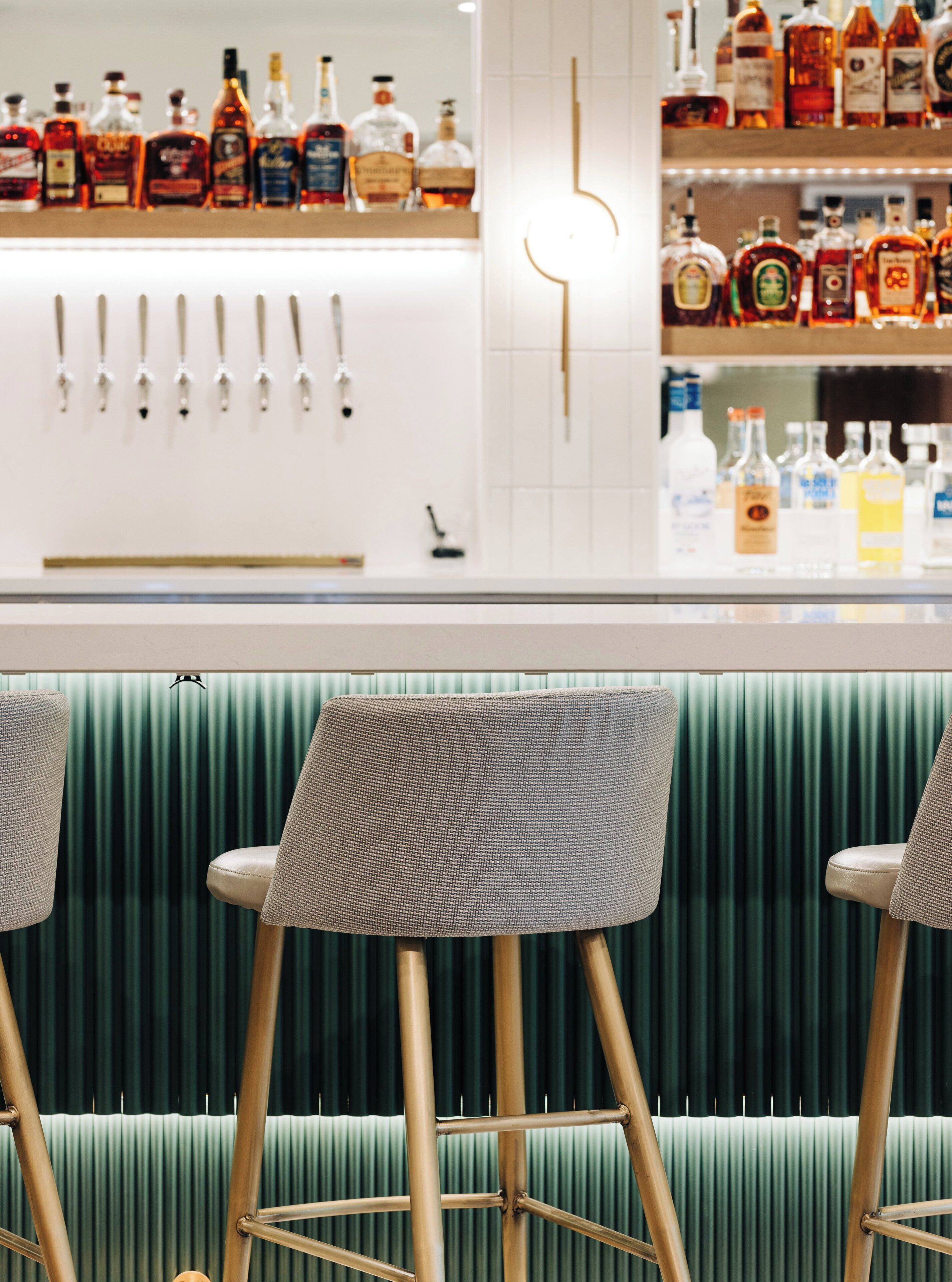 Zona de bar con taburetes y estanterías llenas de botellas de licor.